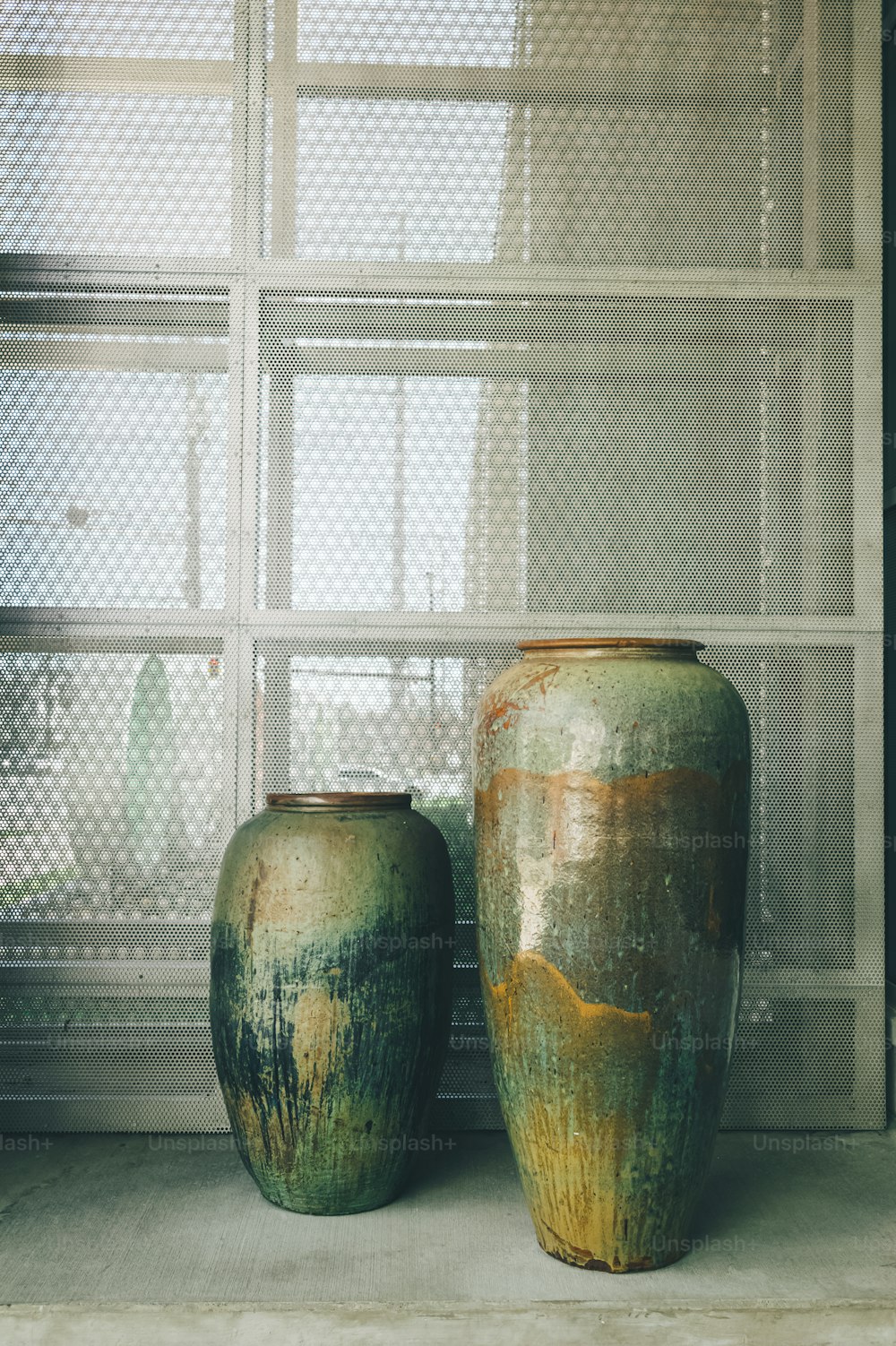 two green vases sitting next to each other in front of a window