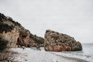 uma pessoa em pé em uma praia rochosa ao lado de um corpo de água