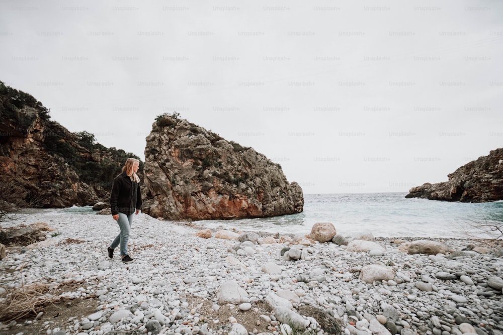 um homem em pé em uma praia rochosa ao lado de um corpo de água