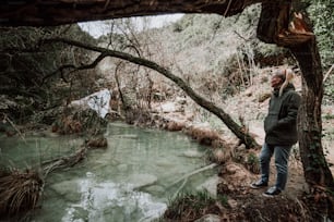 a man standing next to a river in a forest