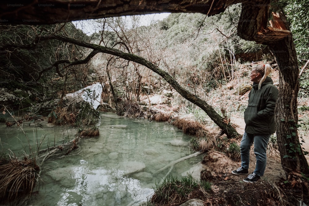 a man standing next to a river in a forest