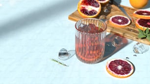 un vaso de jugo de naranja sanguina junto a naranjas sanguinas en rodajas