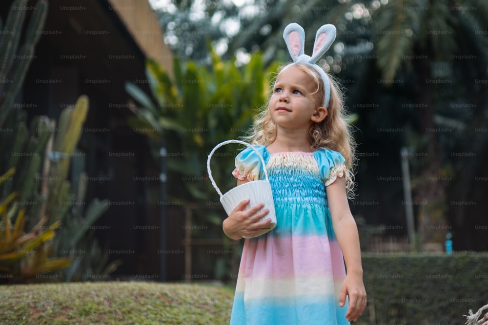 a little girl in a blue and pink dress holding a bucket