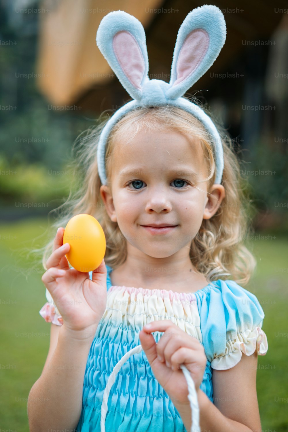 a little girl in a blue dress holding an easter egg