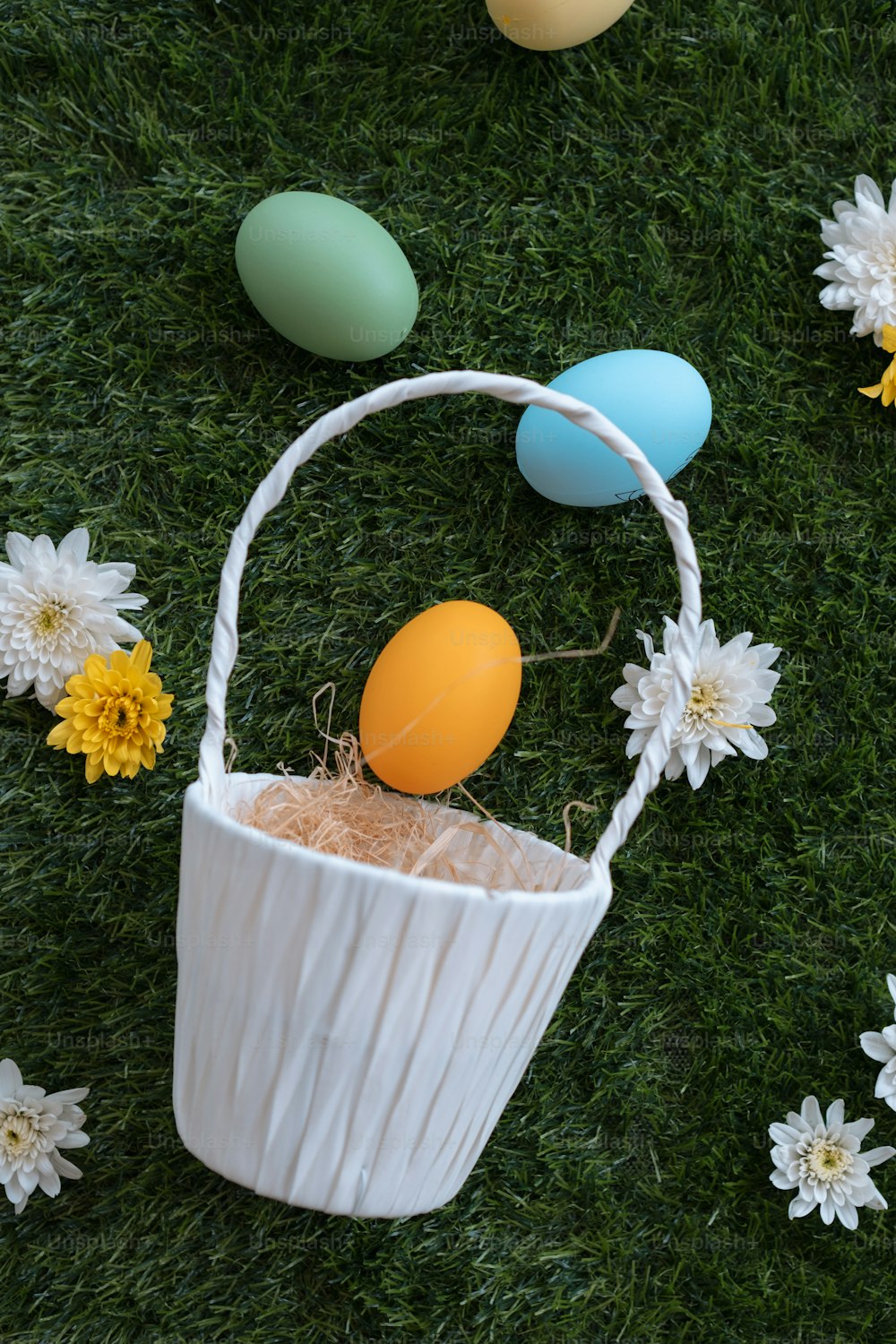 uma cesta de páscoa com ovos e margaridas na grama