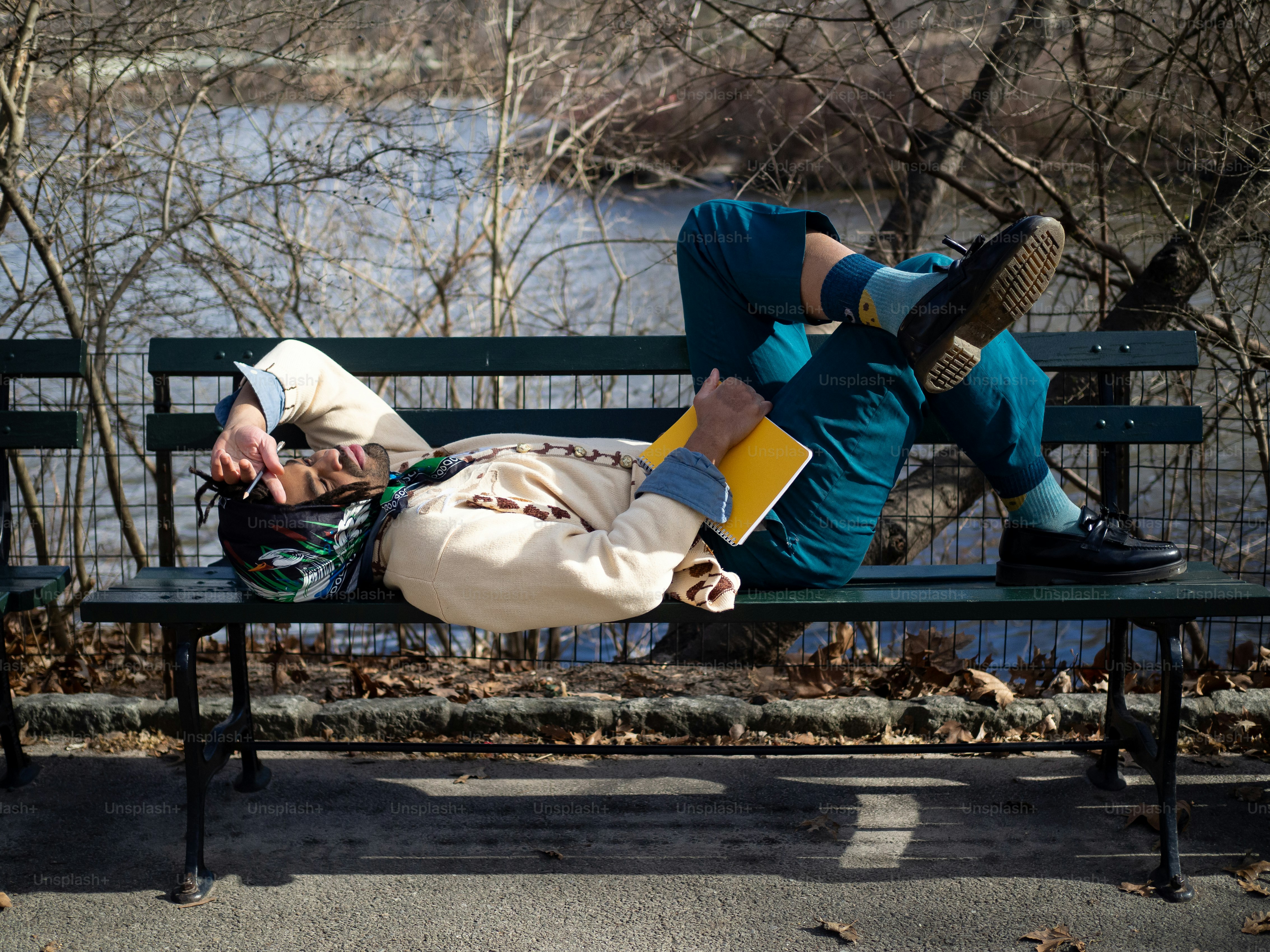 a man laying on top of a green bench next to a river