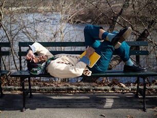 a man laying on top of a green bench next to a river
