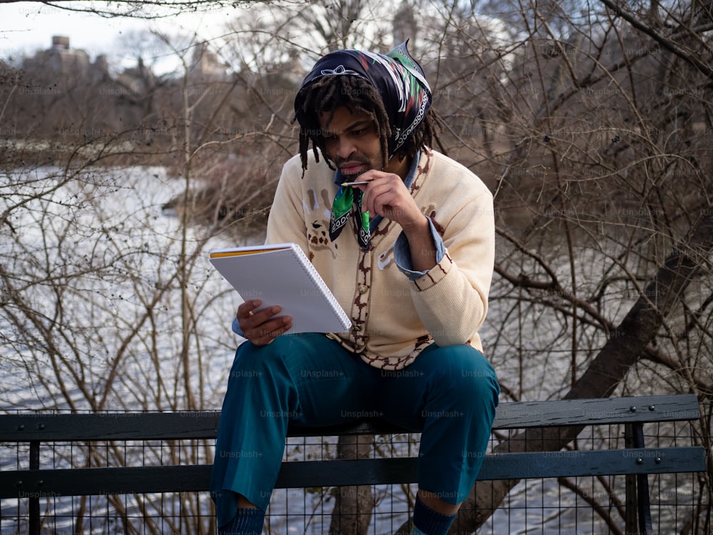 a man with dreadlocks sitting on a bench reading a book