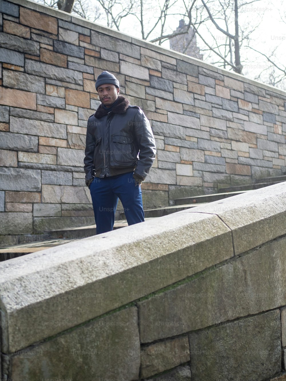 Un hombre de pie junto a un muro de piedra