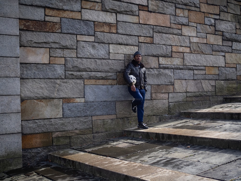 una persona appoggiata a un muro di pietra