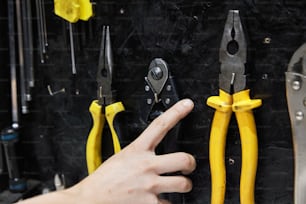 a person pointing at a bunch of pliers hanging on a wall