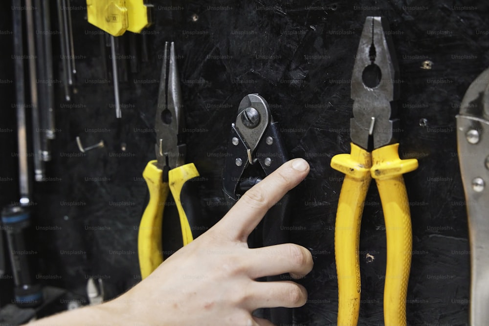 a person pointing at a bunch of pliers hanging on a wall