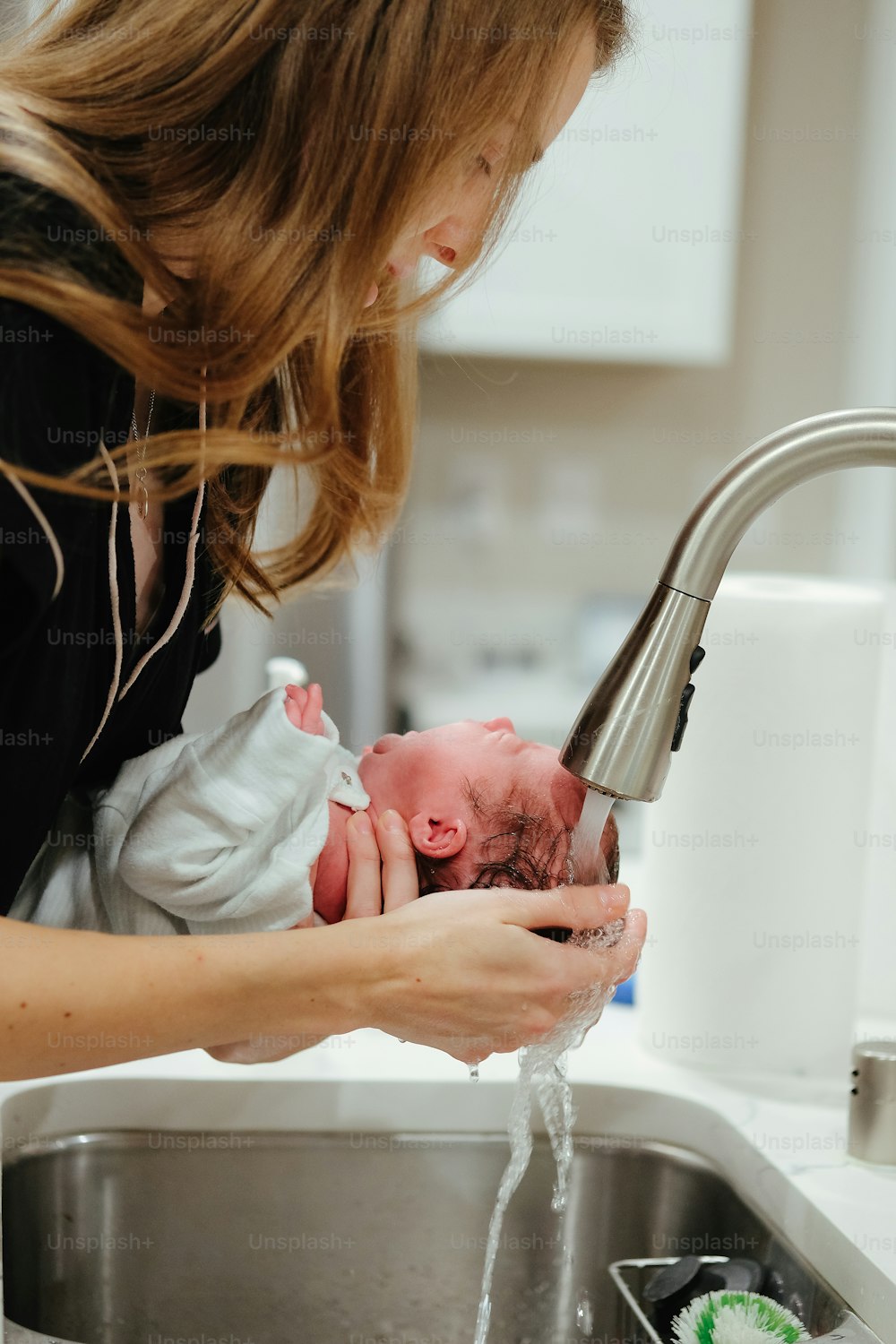 uma mulher que lava um bebê em uma pia