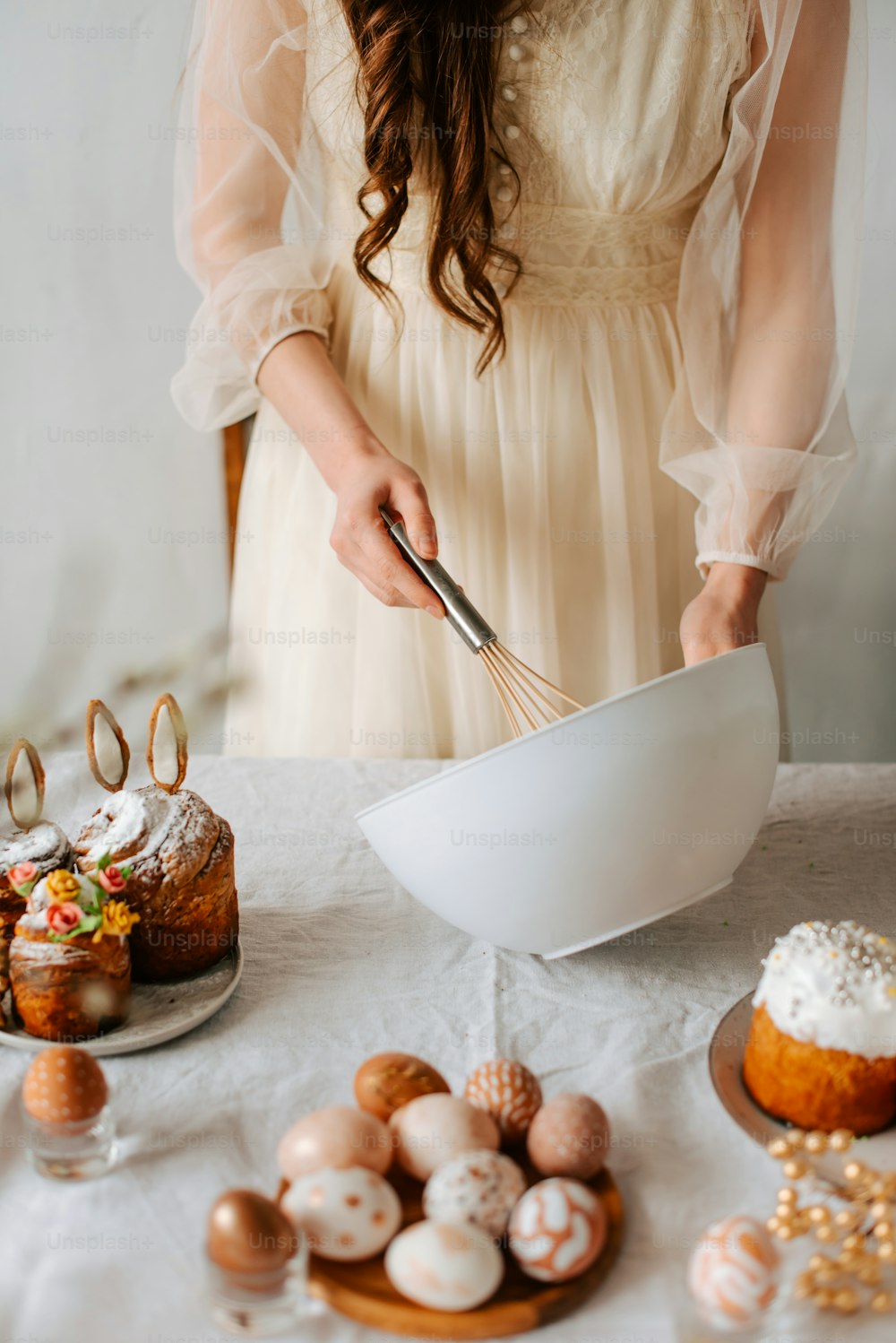 a woman in a white dress mixing a bowl with a whisk