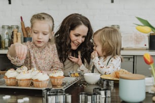 a woman and two children are looking at cupcakes