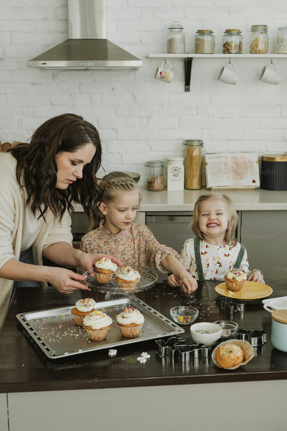 a woman and two children are making cupcakes