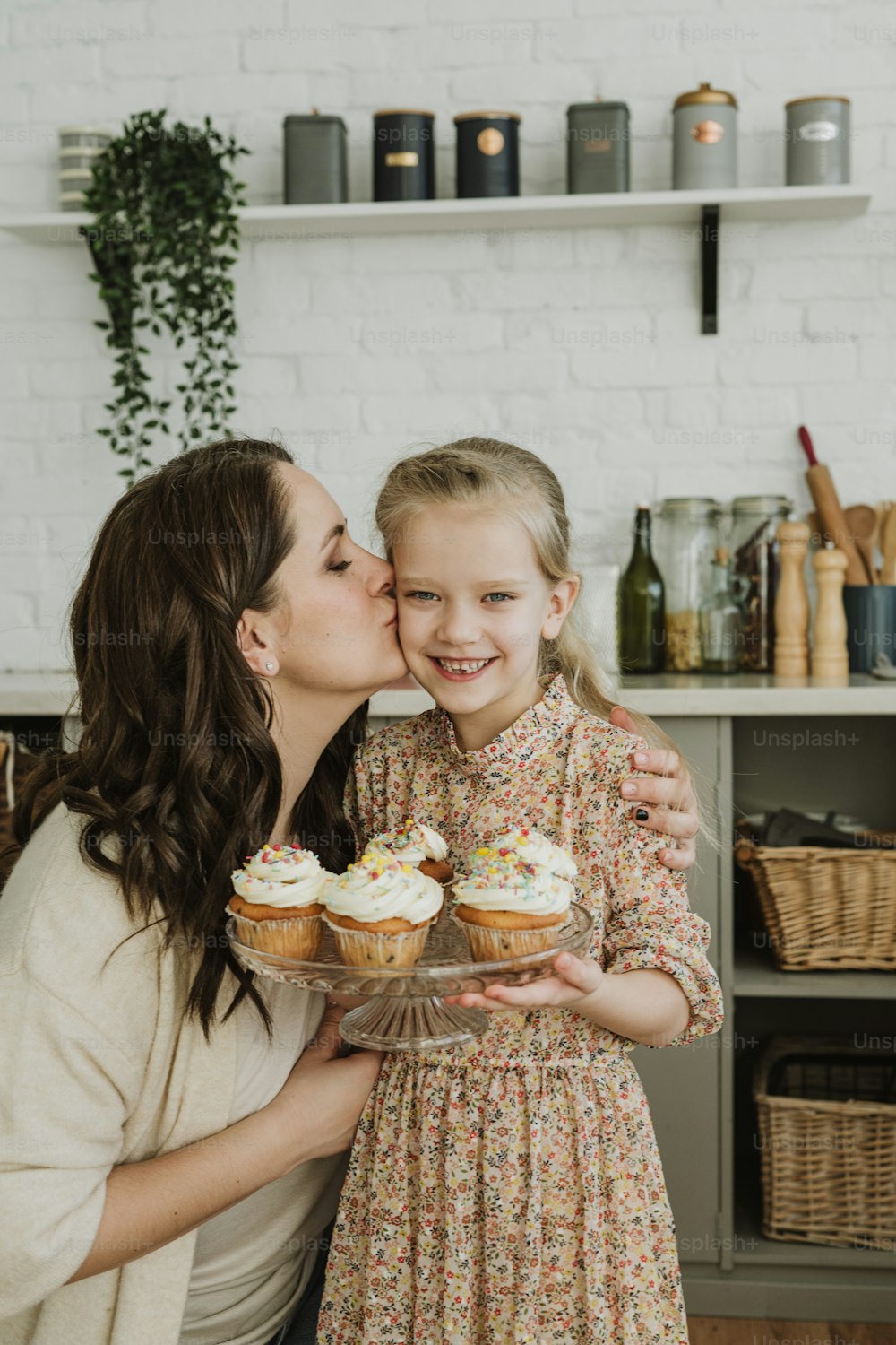 uma mulher beijando uma menina pequena segurando um prato de cupcakes