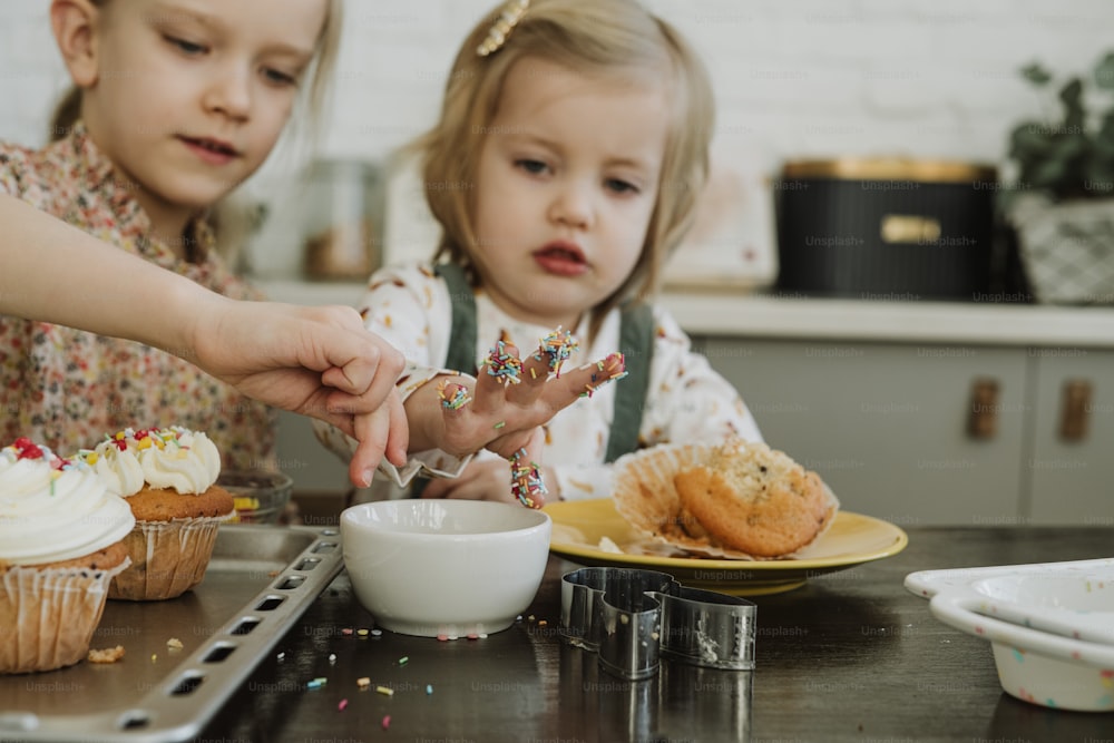 duas meninas sentadas em uma mesa com cupcakes