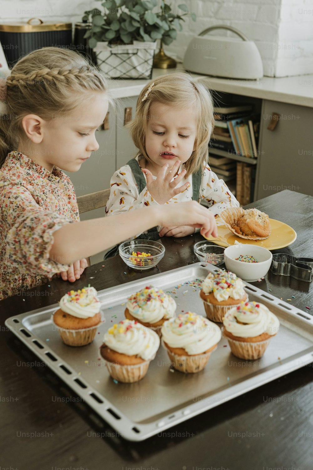 two little girls sitting at a table with cupcakes