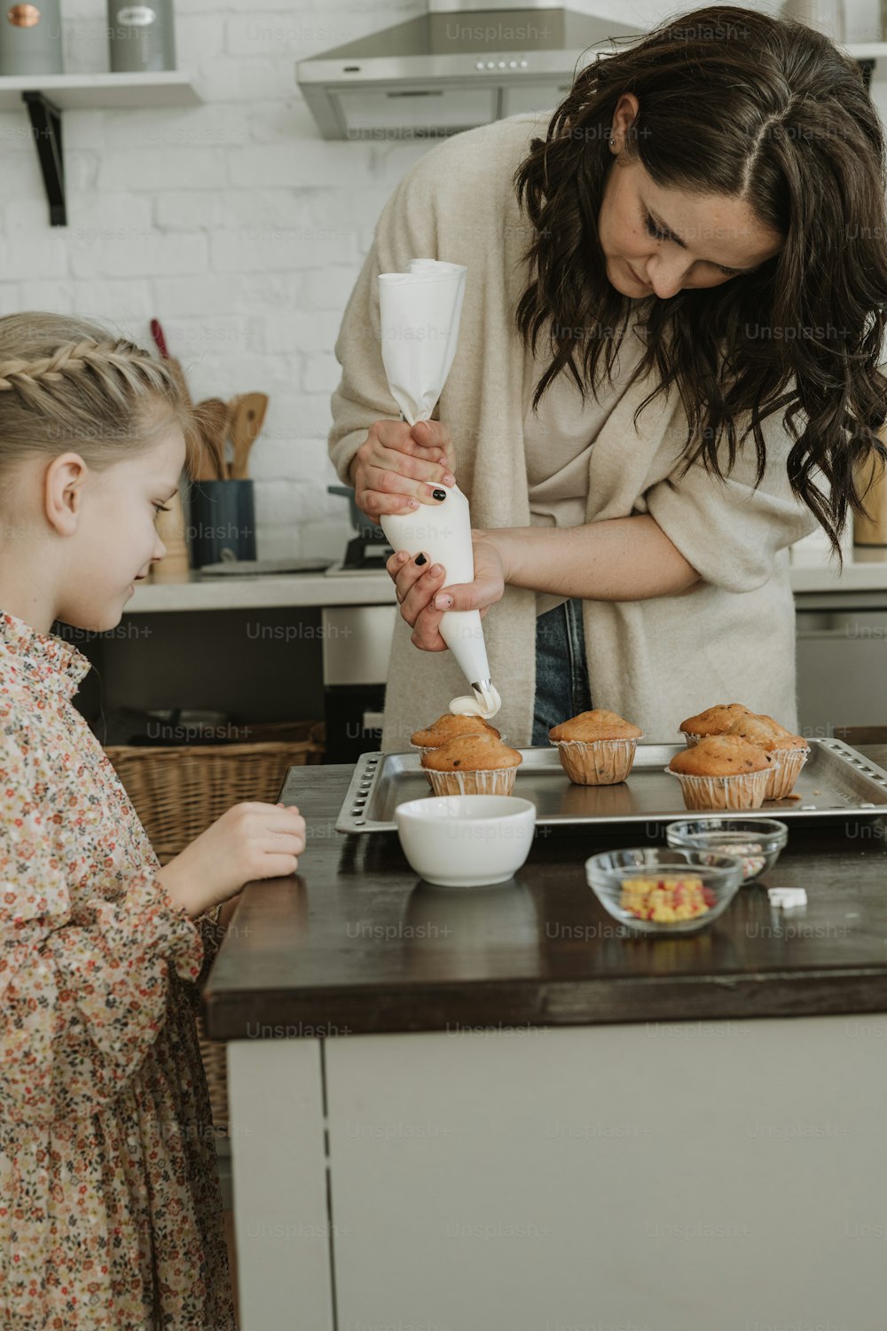 a woman and a little girl making cupcakes in a kitchen