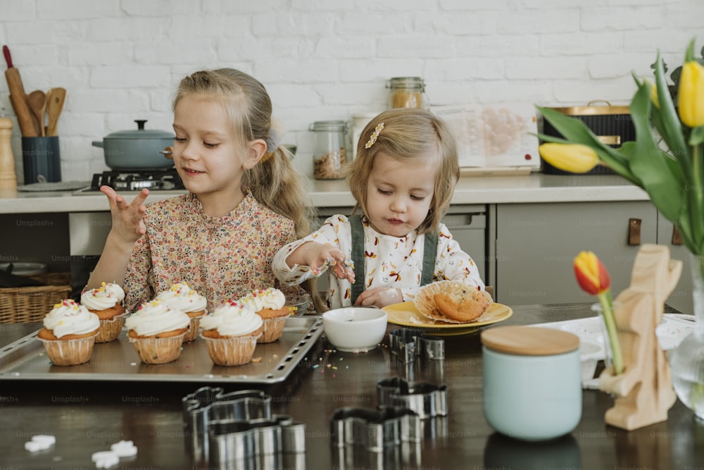 Zwei kleine Mädchen sitzen an einem Tisch mit Cupcakes