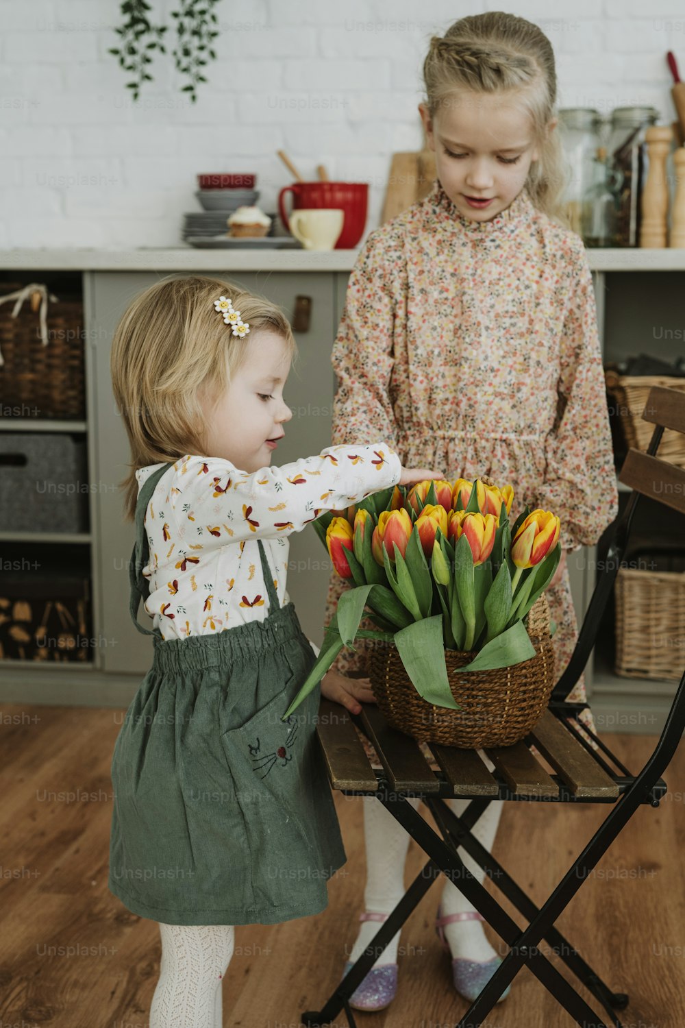 two little girls standing next to each other near a basket of tulips