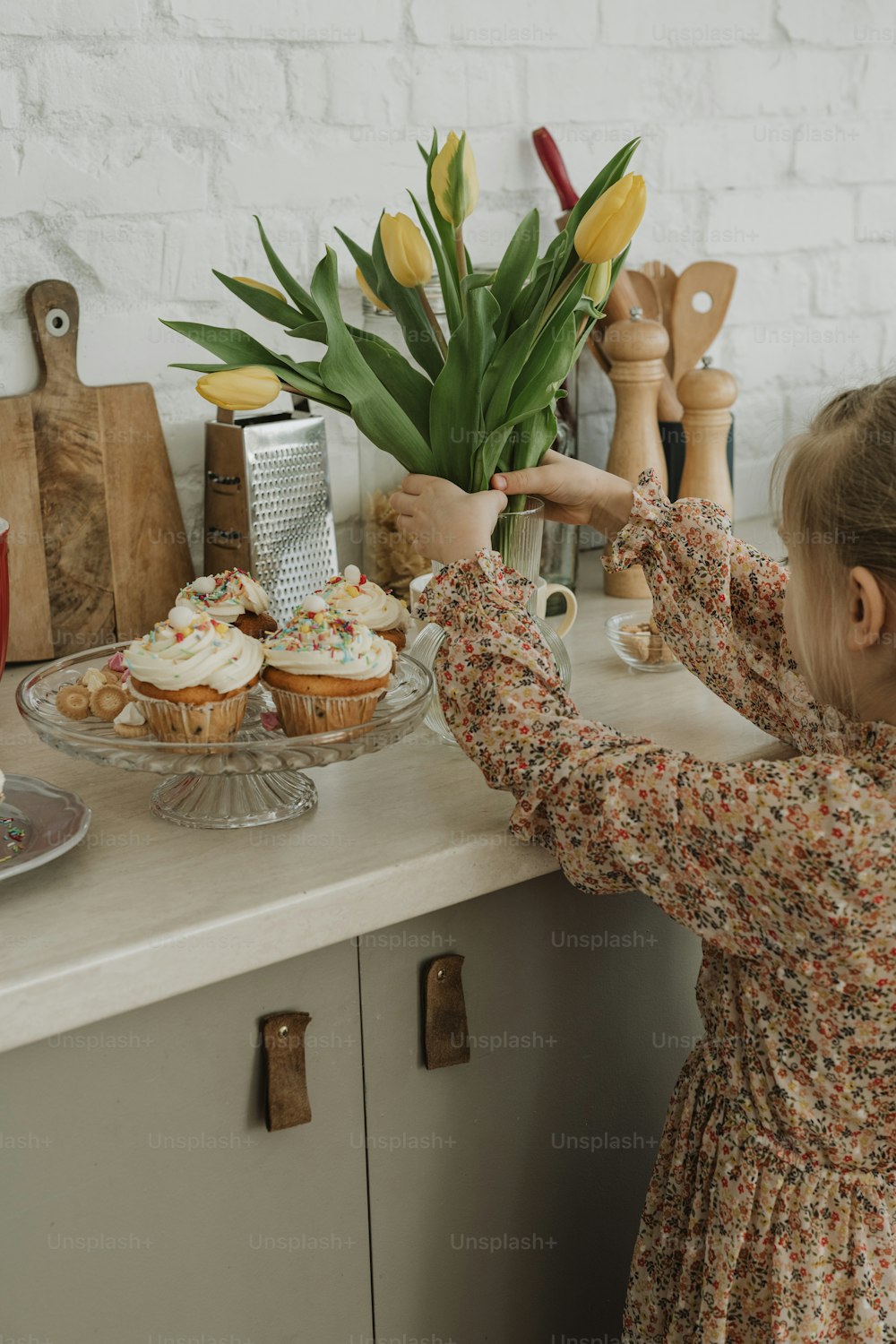 a little girl reaching for some cupcakes on a counter