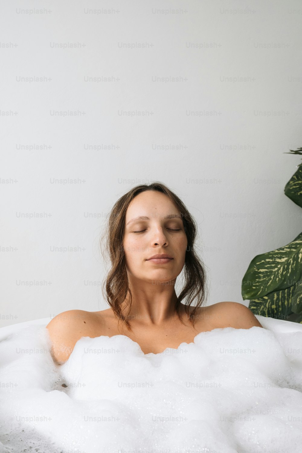 uma mulher sentada em um banho de espuma com os olhos fechados