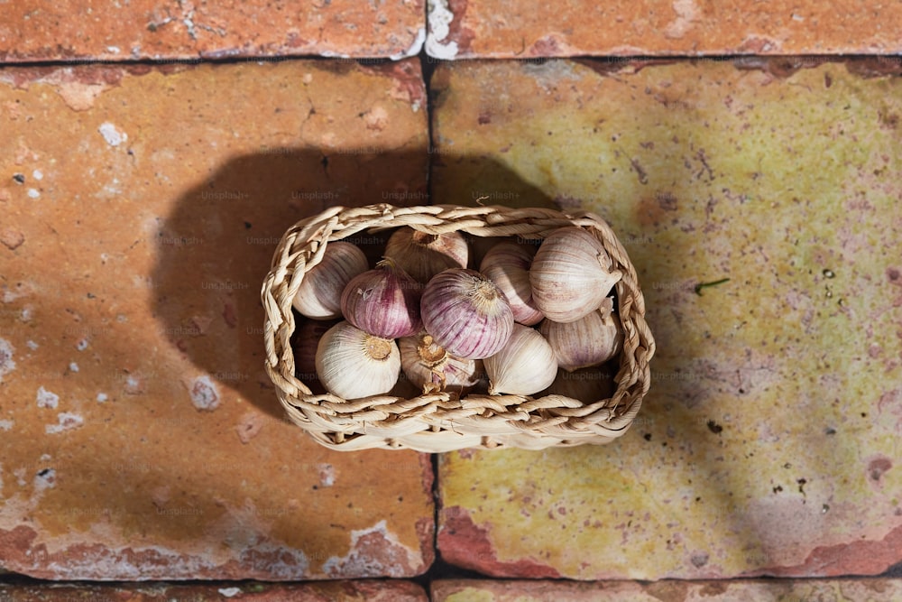 a basket filled with garlic sitting on top of a brick floor