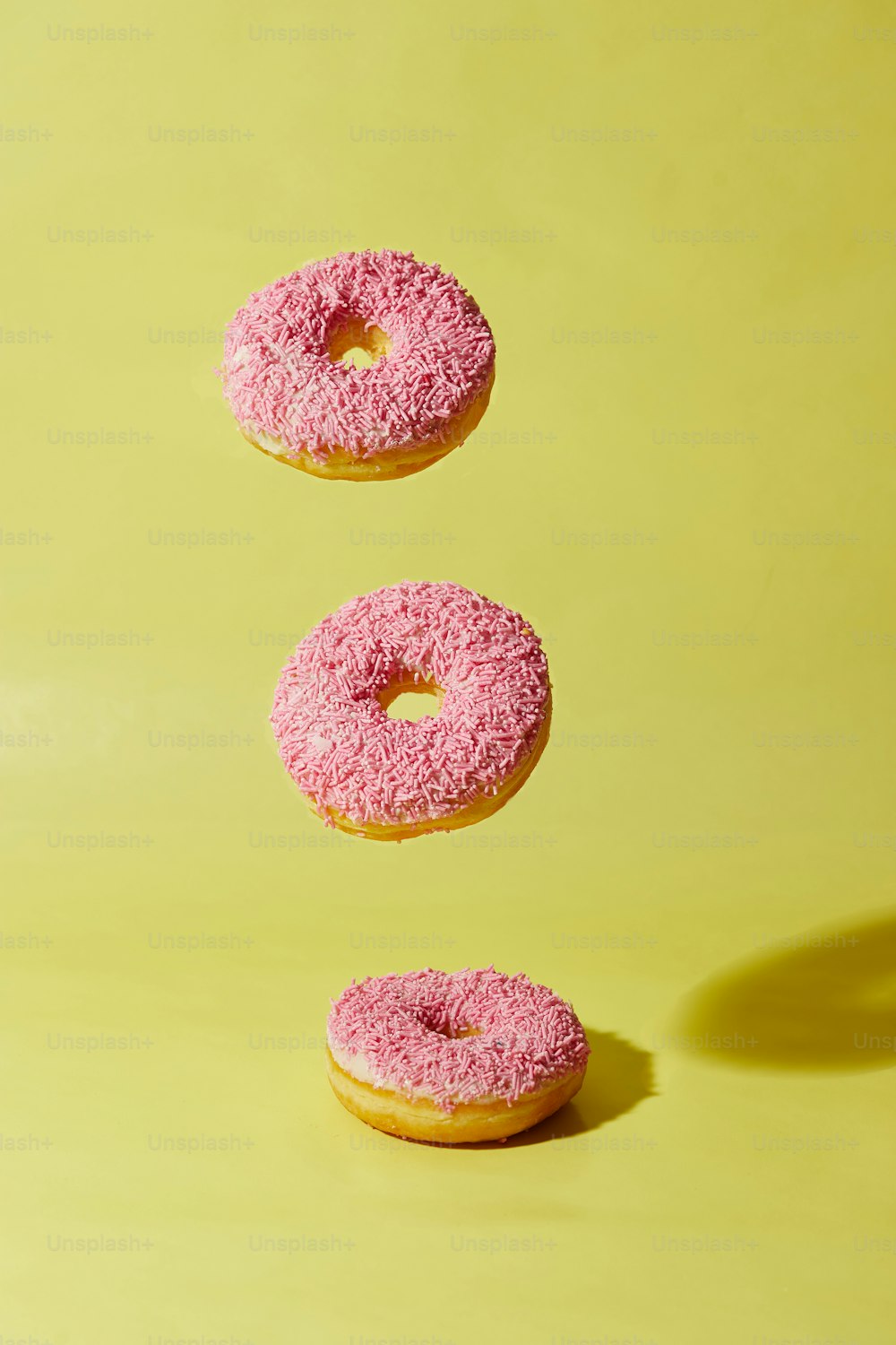 three donuts with pink icing are flying in the air