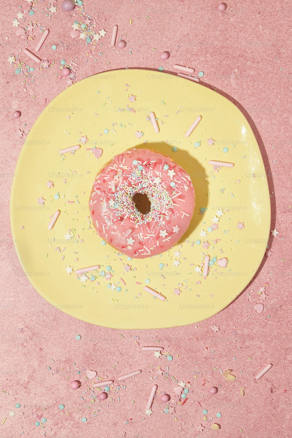 ein rosa Donut mit Streuseln auf einem gelben Teller