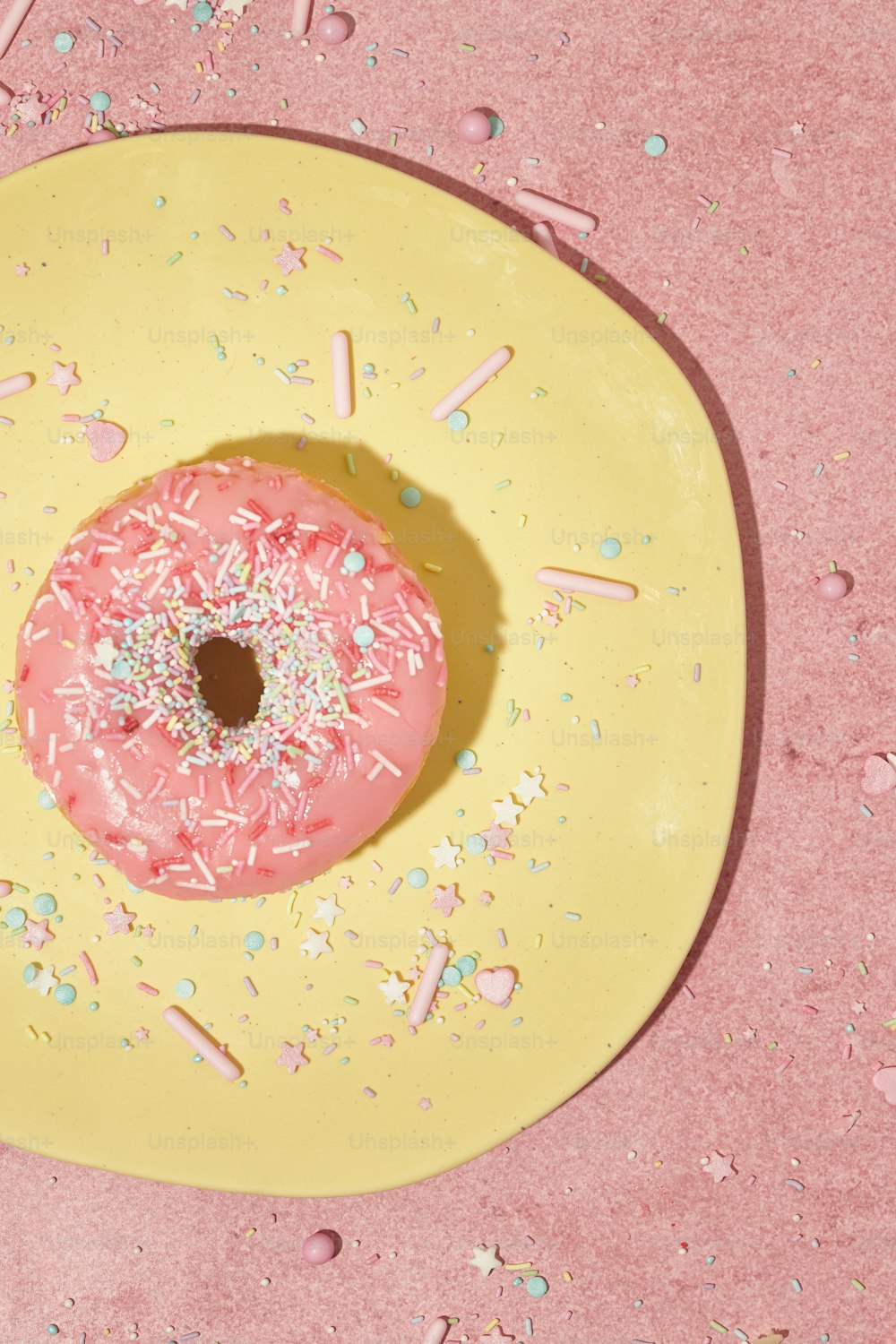 ein rosa gefrosteter Donut mit Streuseln auf einem gelben Teller