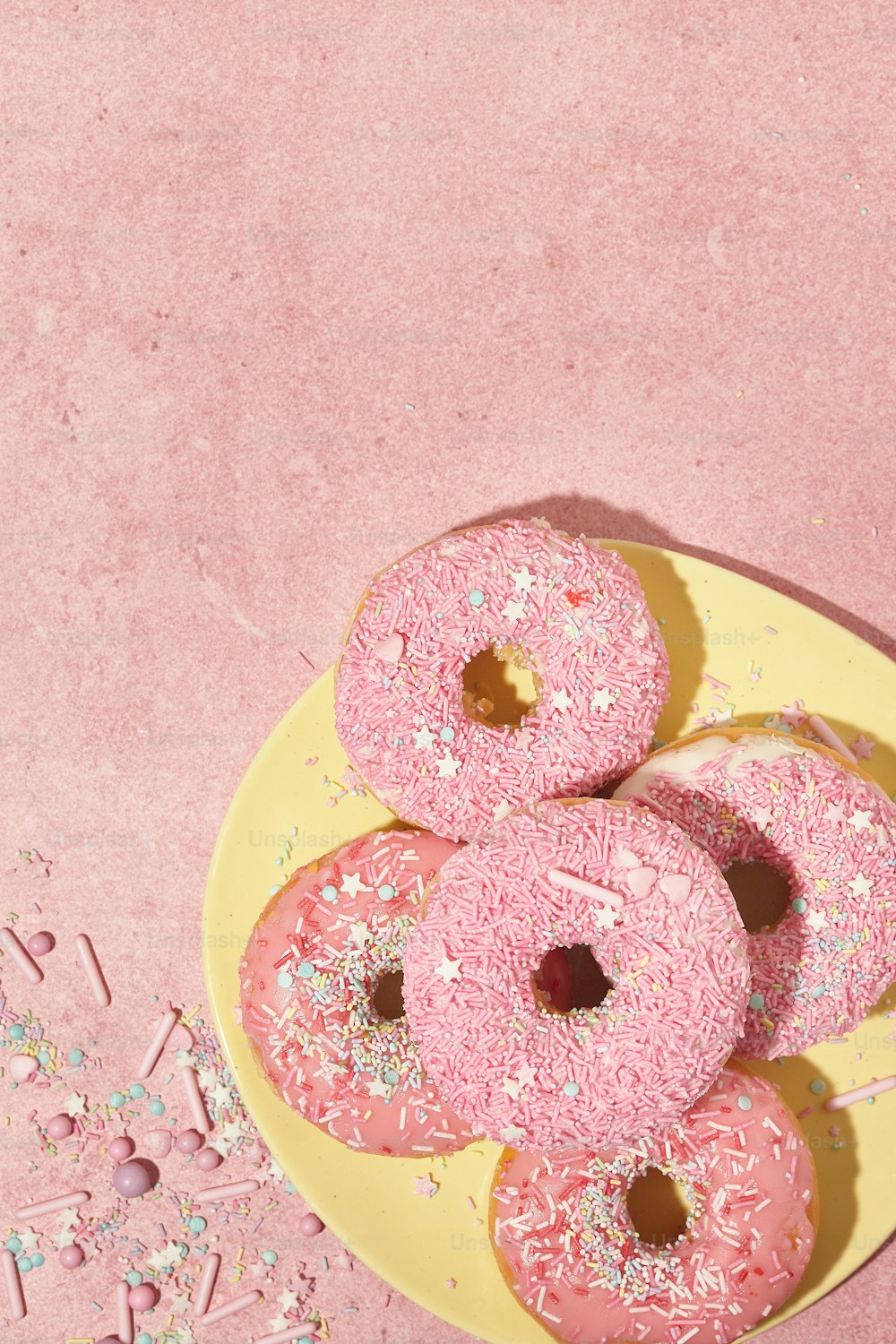 a yellow plate topped with pink donuts covered in sprinkles