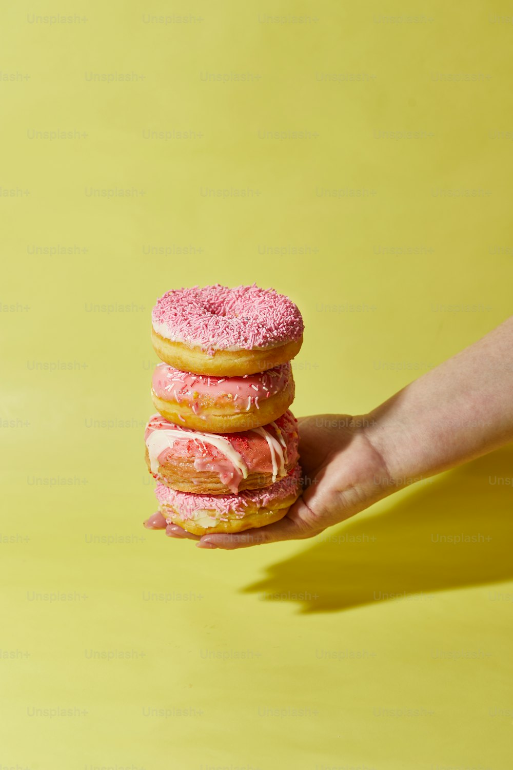 uma mão segurando uma pilha de donuts cor-de-rosa