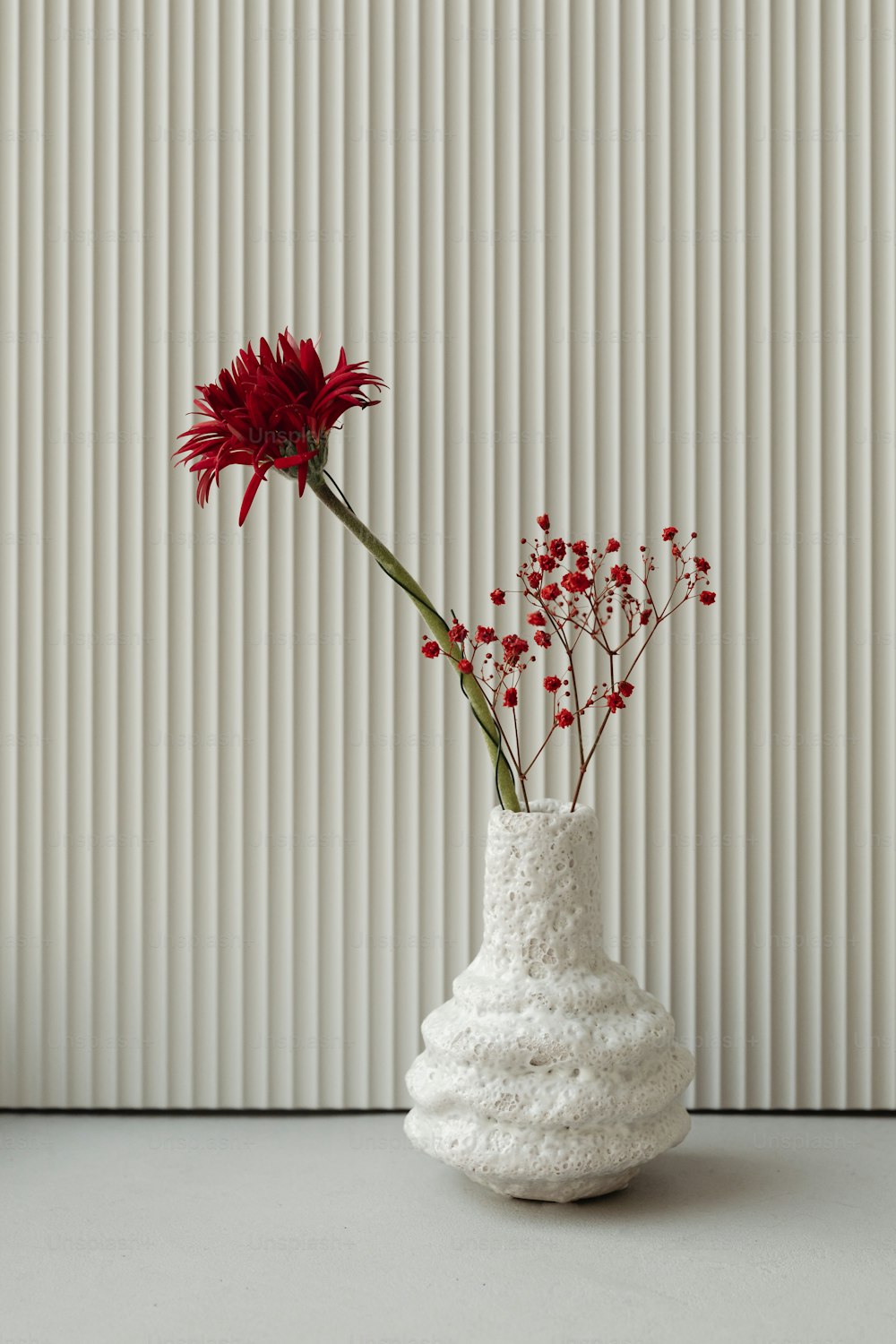a white vase with a red flower in it