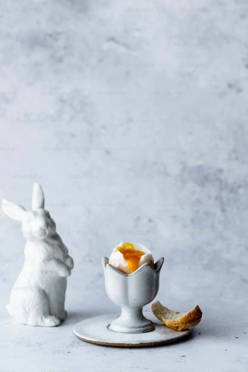 Una figura de conejito blanco sentada junto a un tazón de huevos