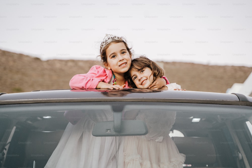 two little girls in a wedding dress sitting in the back of a car