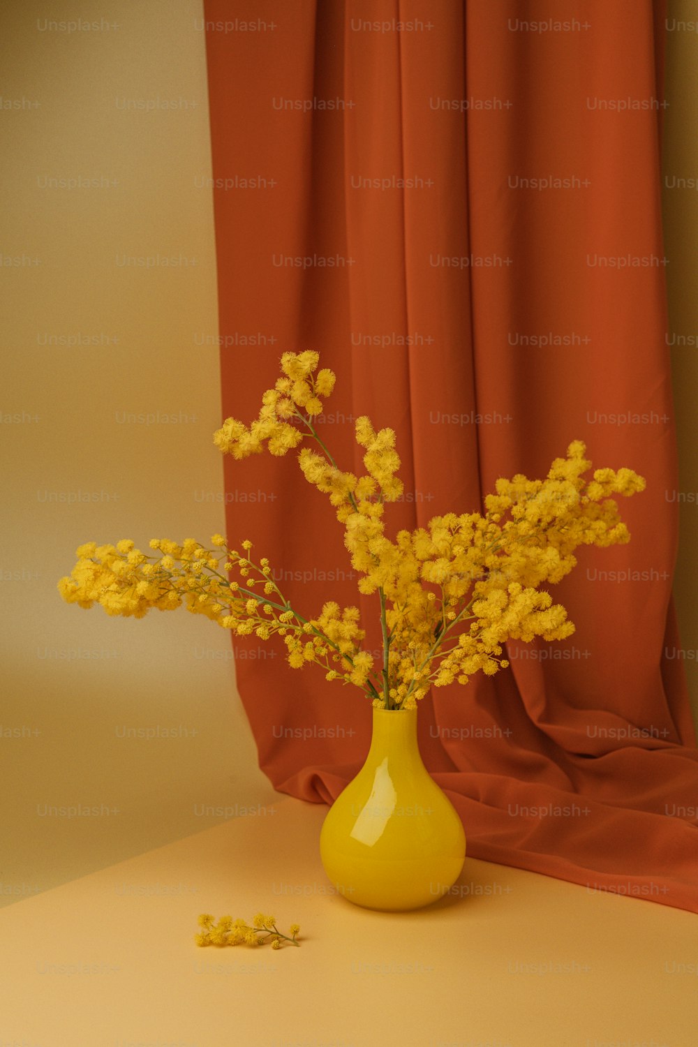 Un jarrón amarillo lleno de flores amarillas sobre una mesa