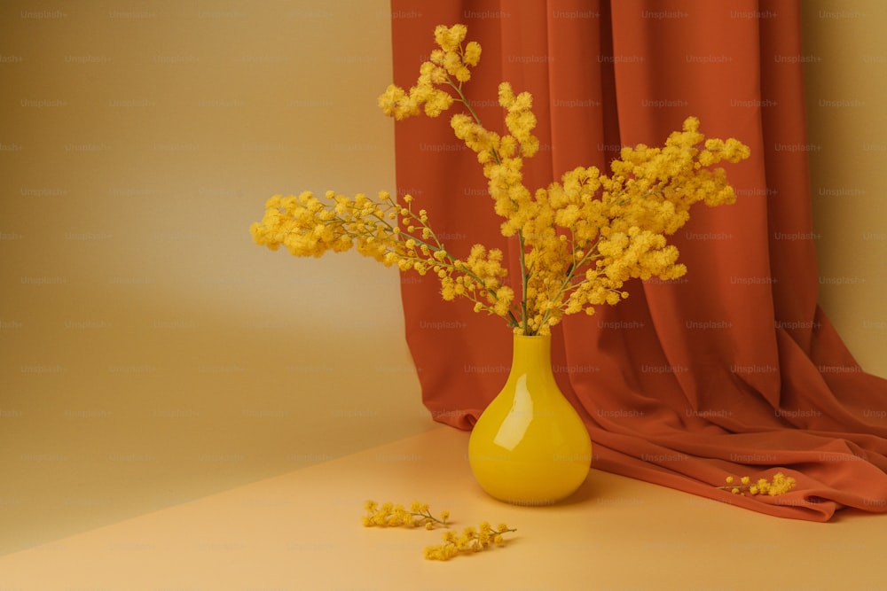 un vase jaune rempli de fleurs jaunes à côté d’un rideau rouge