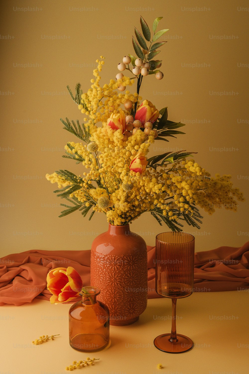 ワイングラスの横にある黄色い花でいっぱいの花瓶