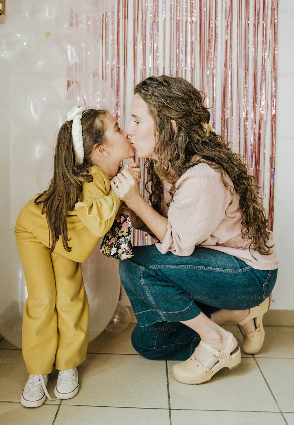 a woman kneeling down to kiss a little girl