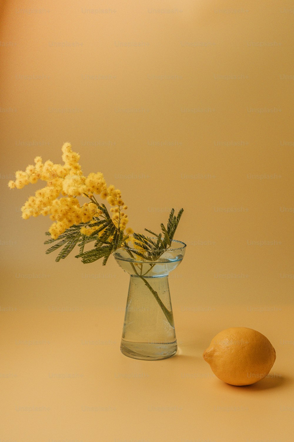 una flor amarilla en un jarrón de vidrio junto a un limón