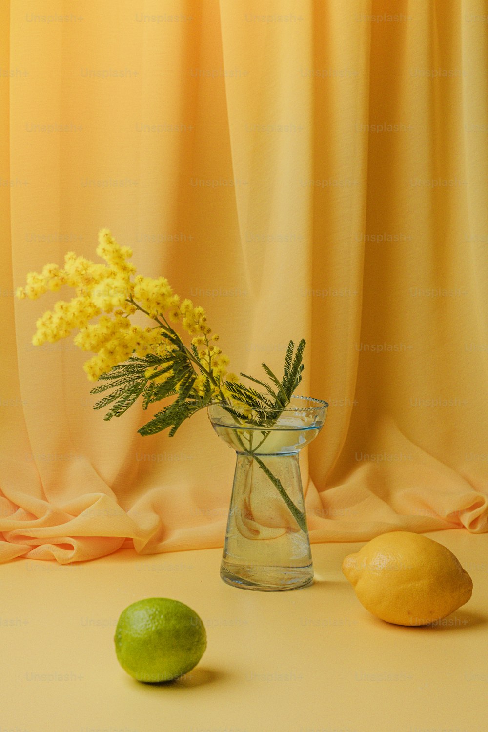 Un jarrón de vidrio lleno de flores amarillas junto a limones