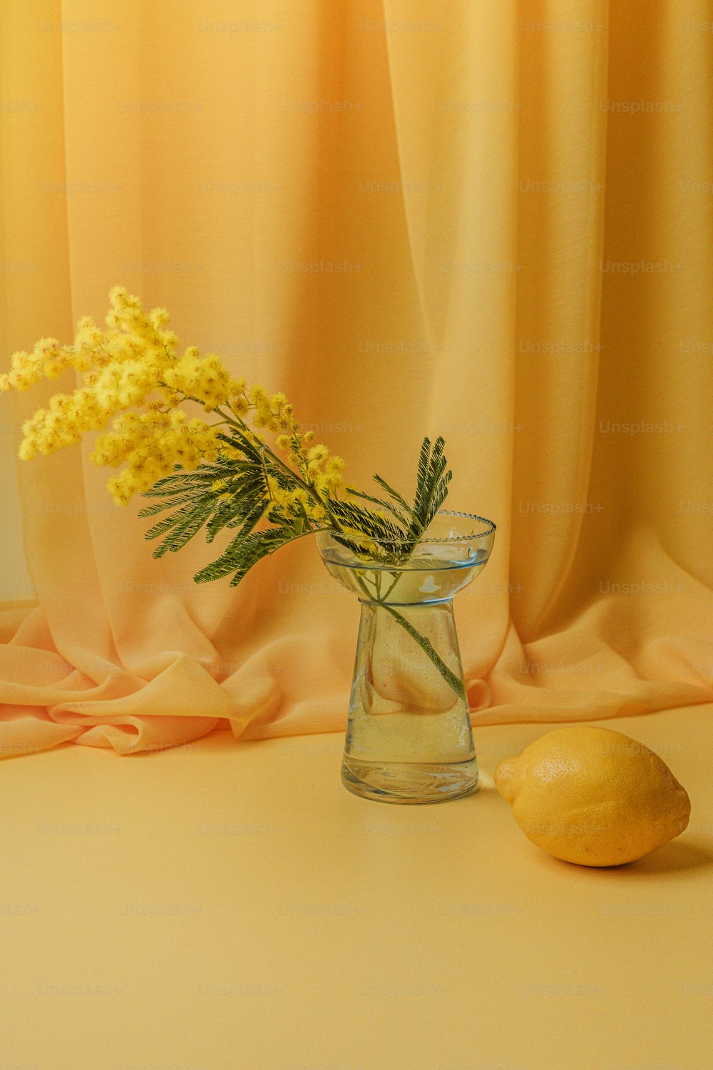um vaso de vidro com flores e um limão em uma mesa