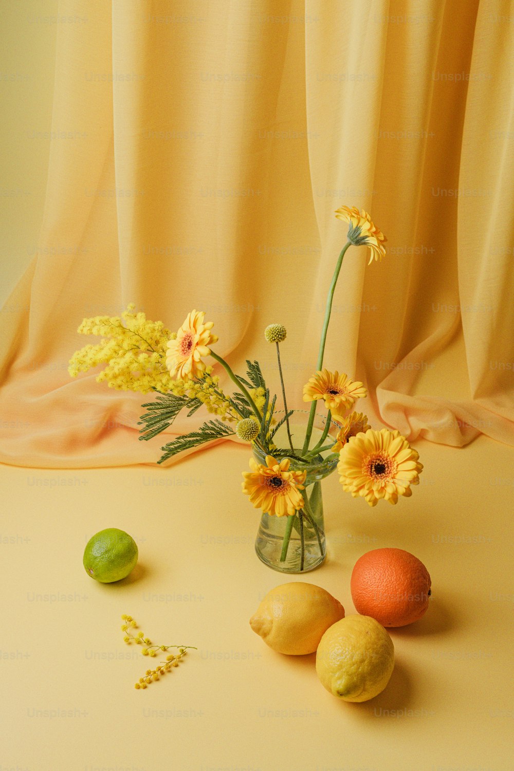 Un jarrón lleno de flores amarillas junto a limones