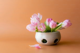 un vaso bianco pieno di fiori rosa in cima a un tavolo