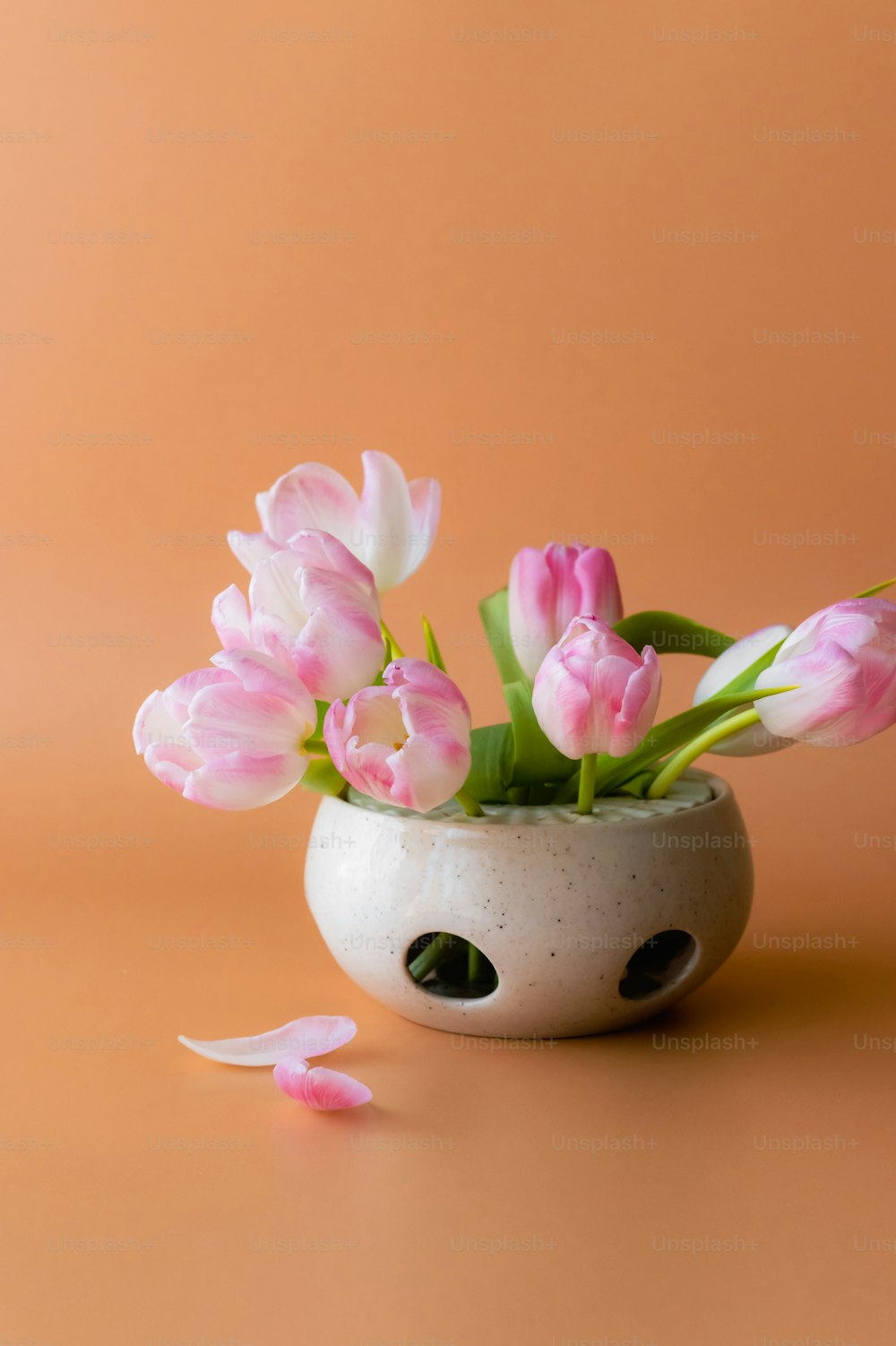 a white vase filled with pink flowers on top of a table