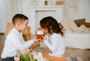 a boy and a girl sitting on the floor eating cupcakes
