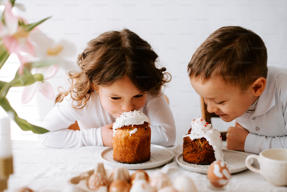 a couple of kids sitting at a table with a cake