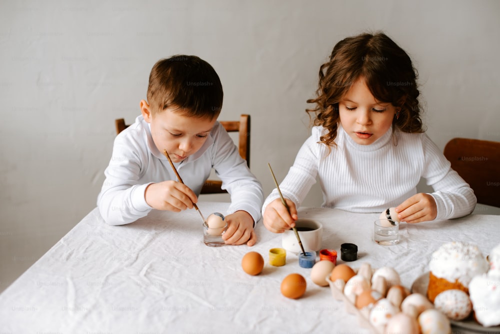a boy and a girl painting eggs on a table
